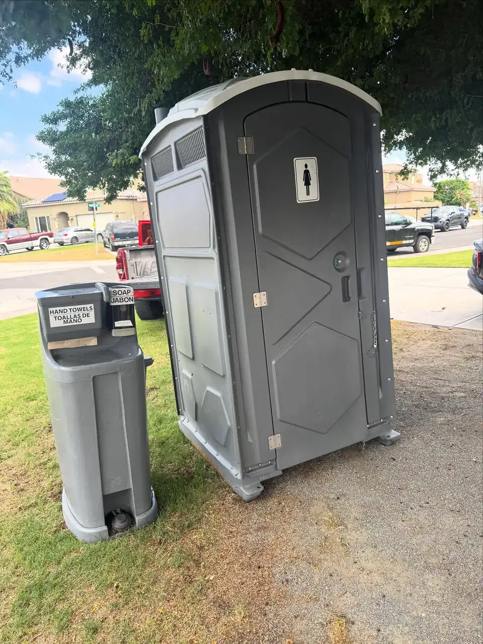 Gray standard porta potty with a separate hand-wash station set on a lawn