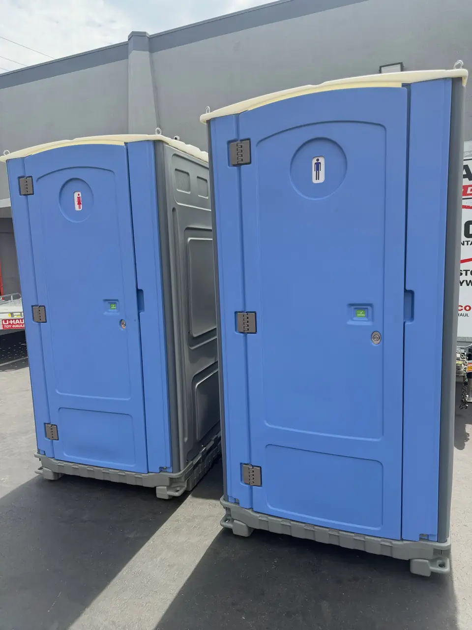 Two blue porta potties on a gravel construction lot